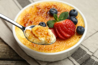 Photo of Taking delicious creme brulee with berries and mint from bowl at wooden table, closeup