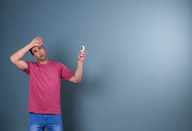 Young man operating air conditioner with remote control on dark background