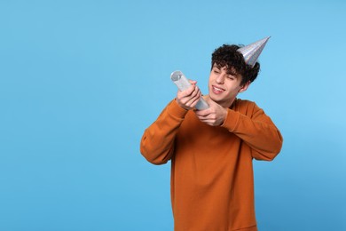 Photo of Handsome young man in party hat with popper on light blue background. Space for text