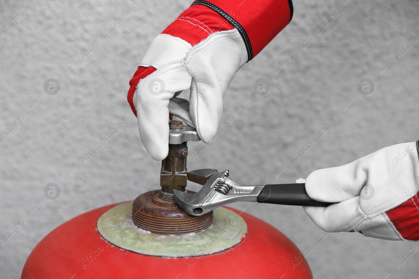 Photo of Worker with adjustable wrench opening red gas cylinder near wall, closeup