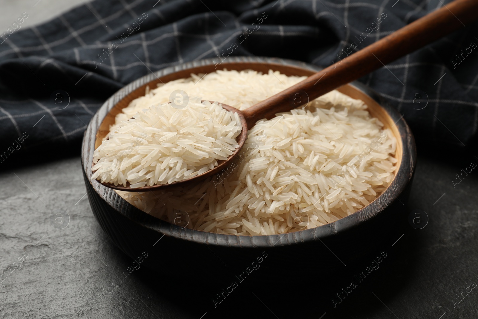 Photo of Raw basmati rice in bowl and spoon on black table, closeup