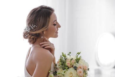 Young bride with elegant hairstyle holding wedding bouquet indoors. Space for text