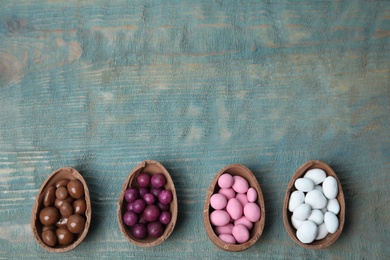 Photo of Broken chocolate Easter eggs with colorful candies on blue wooden table, flat lay. Space for text