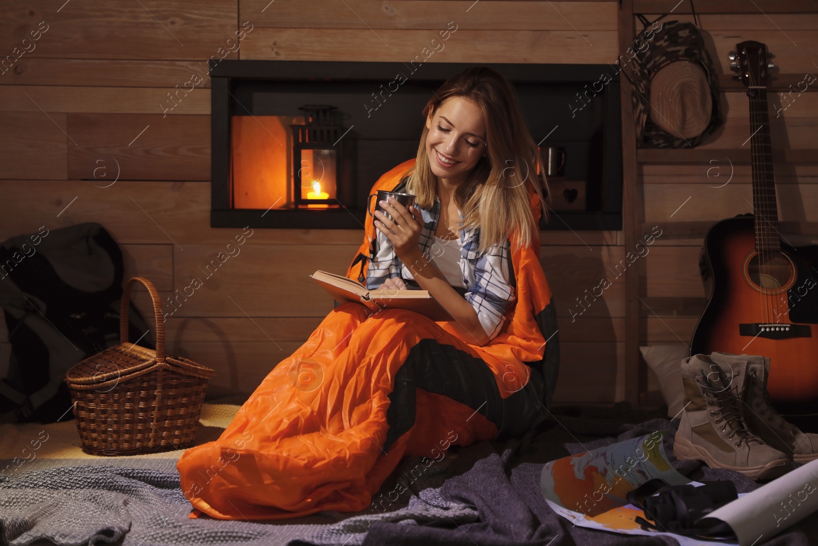 Photo of Young woman in sleeping bag with mug reading book indoors