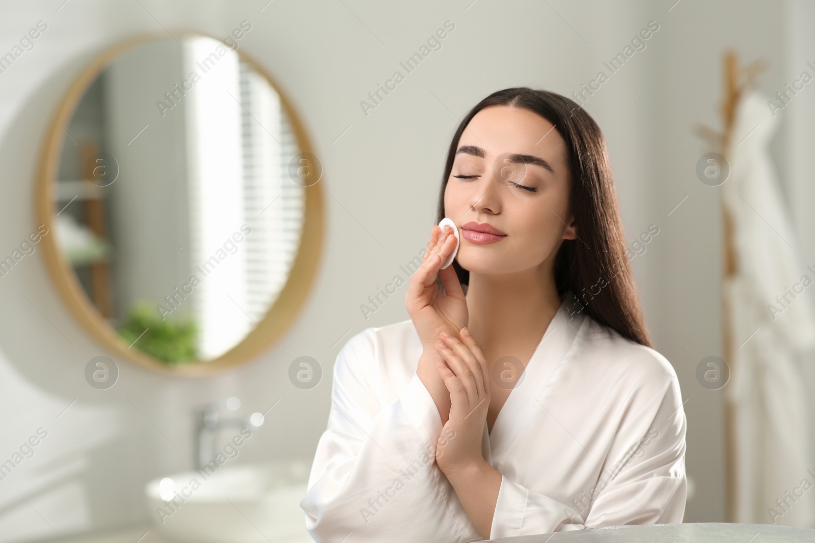 Photo of Beautiful woman removing makeup with cotton pad indoors