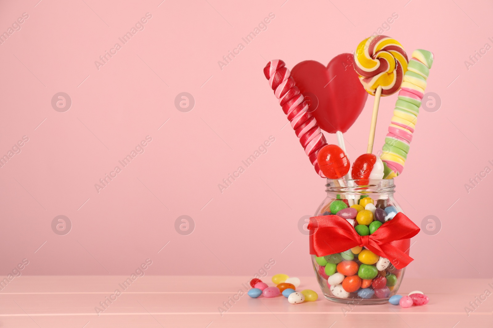 Photo of Jar with different delicious candies on pink wooden table, space for text
