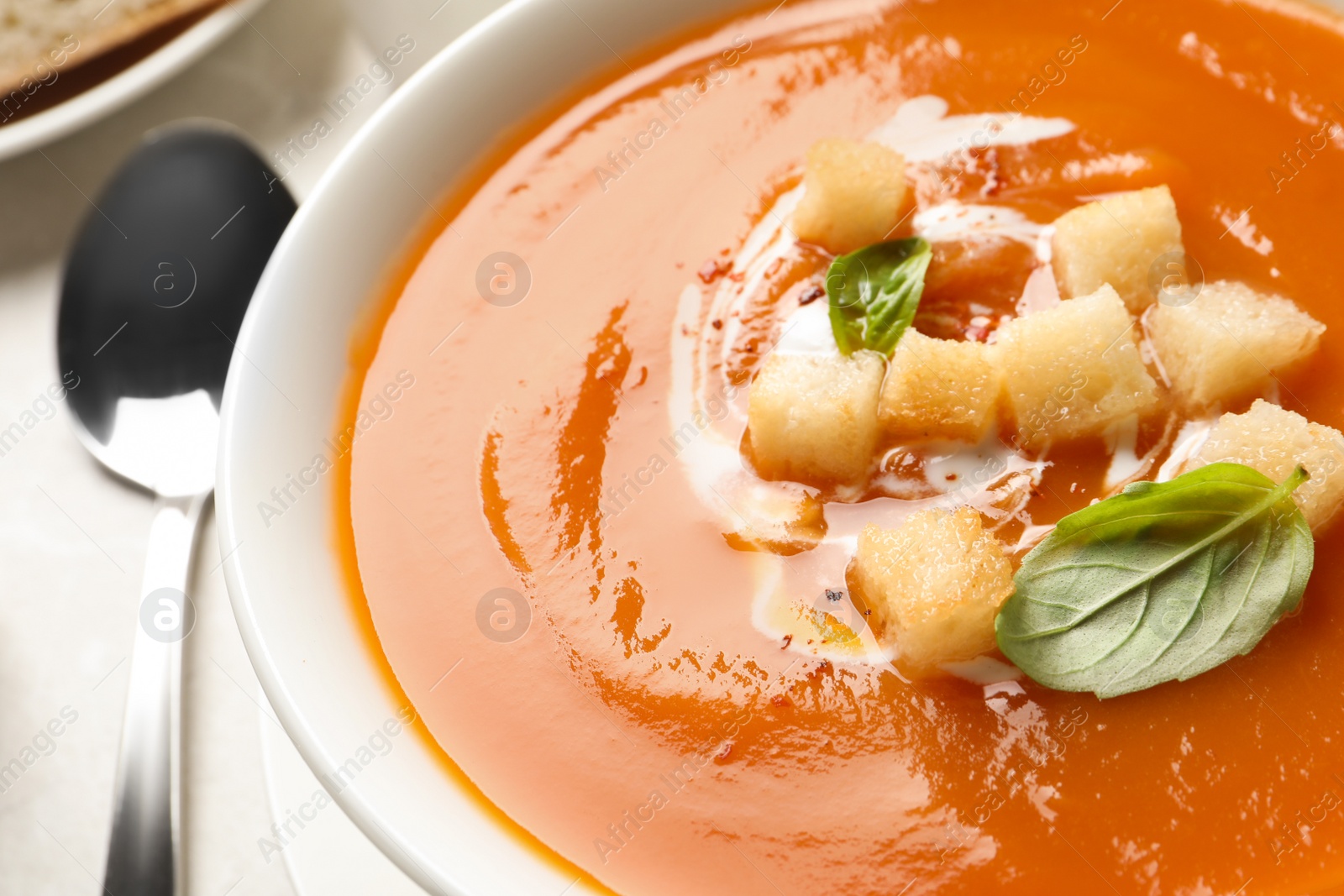 Photo of Bowl of sweet potato soup with croutons and basil on table, closeup