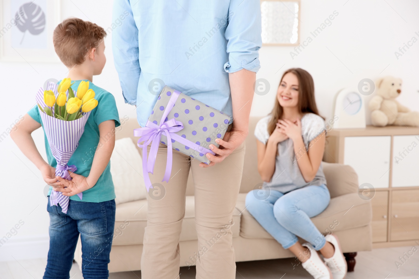 Photo of Husband and son hiding flowers and gift behind their backs at home