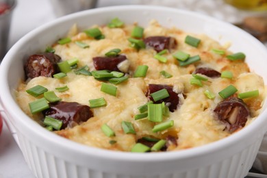 Photo of Tasty sausage casserole with green onion in baking dish on white table, closeup