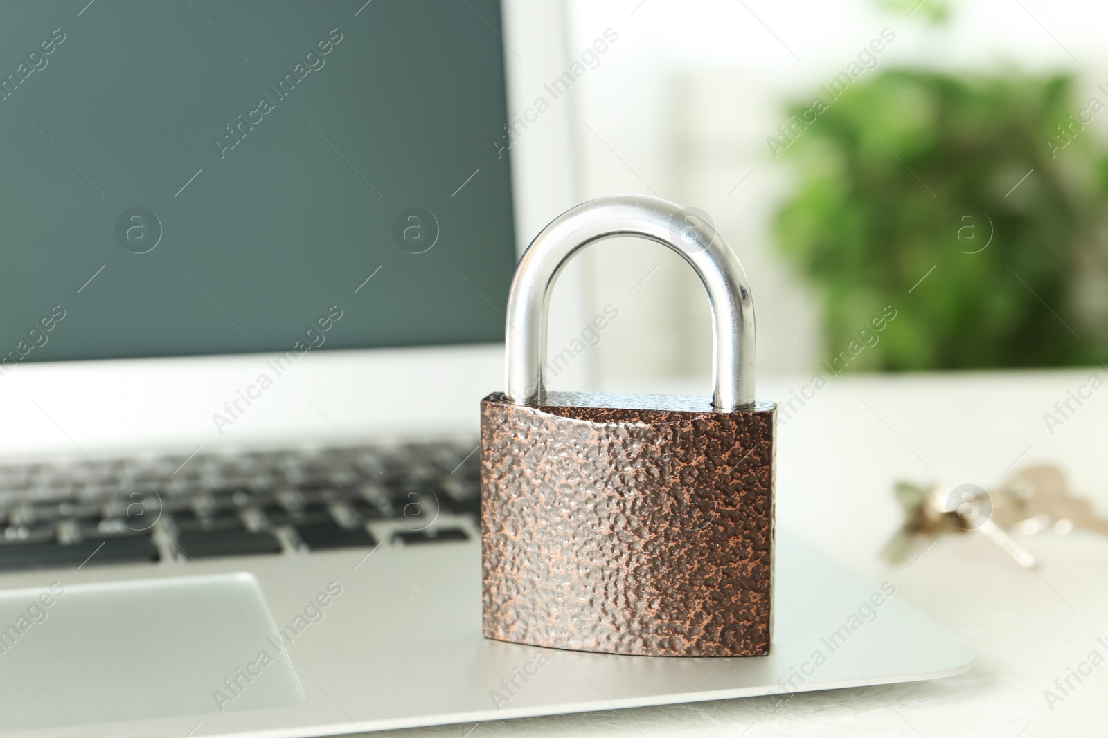 Photo of Metal lock and laptop on table, closeup. Protection from cyber attack