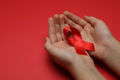Photo of Little girl holding red ribbon on bright background, closeup with space for text. AIDS disease awareness