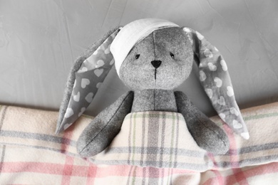 Photo of Toy bunny with bandage lying under blanket on grey background, top view. Children's hospital