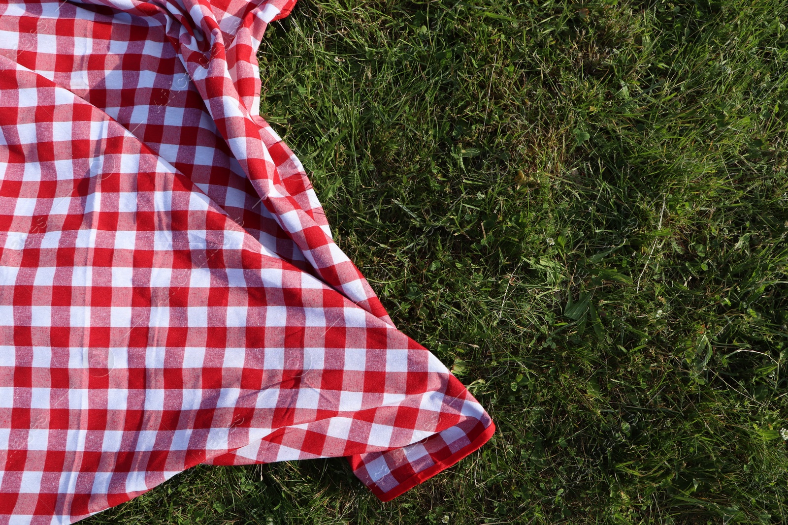 Photo of Checkered picnic tablecloth on fresh green grass, top view. Space for text