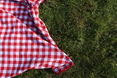 Photo of Checkered picnic tablecloth on fresh green grass, top view. Space for text