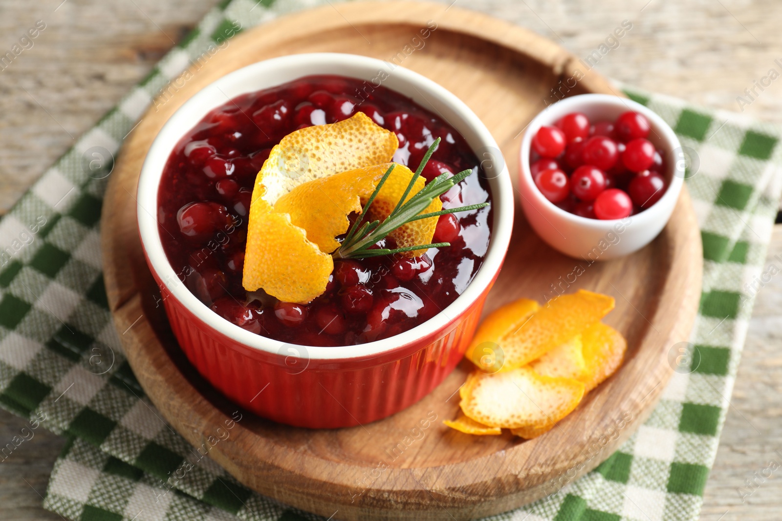 Photo of Cranberry sauce in bowl, fresh berries, rosemary and orange peels on table, closeup