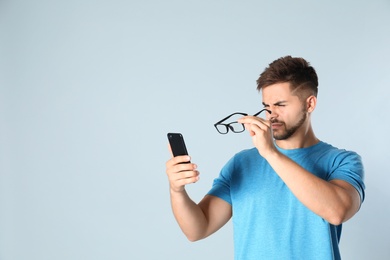 Photo of Young man with vision problems using smartphone on grey background, space for text