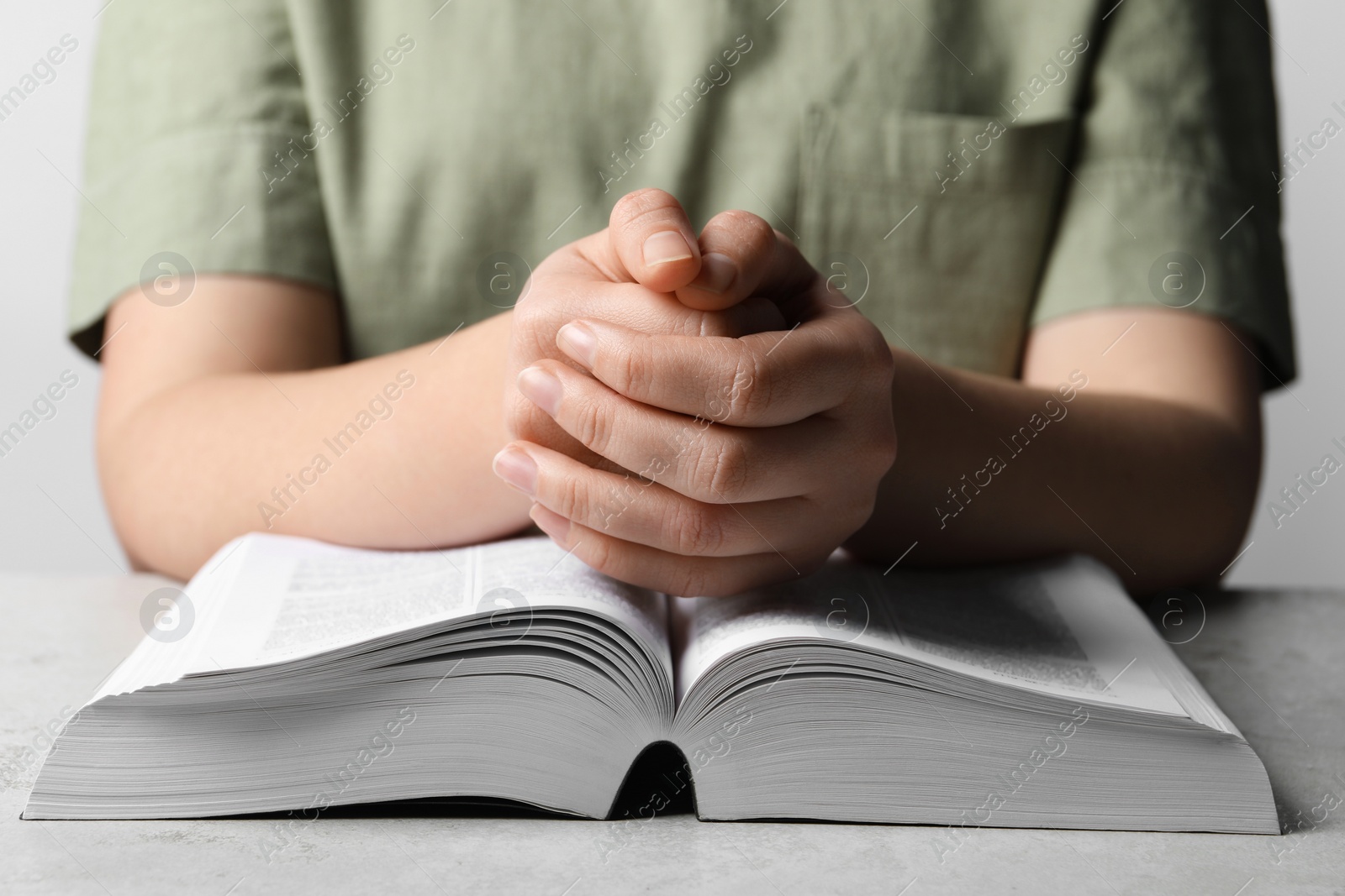 Photo of Woman holding hands clasped while praying over Bible at grey textured table, closeup