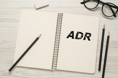 Image of Alternative dispute resolution. Notebook with abbreviation ADR, pencils, eraser and glasses on white wooden table, flat lay