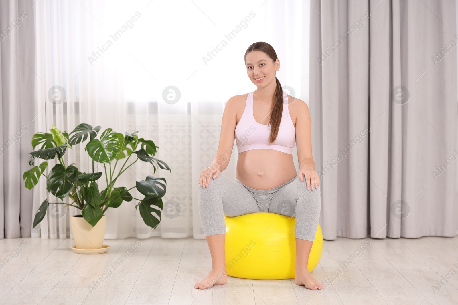 Photo of Pregnant woman sitting on fitness ball in room. Home yoga