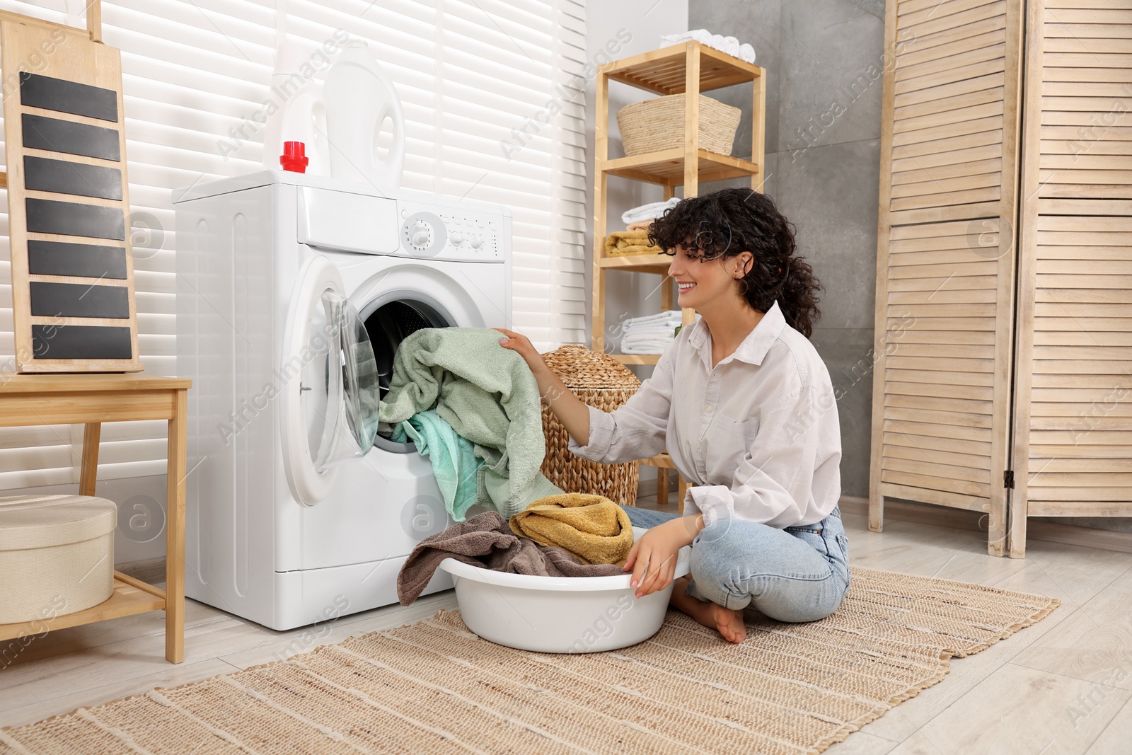 Photo of Woman taking laundry out of washing machine indoors