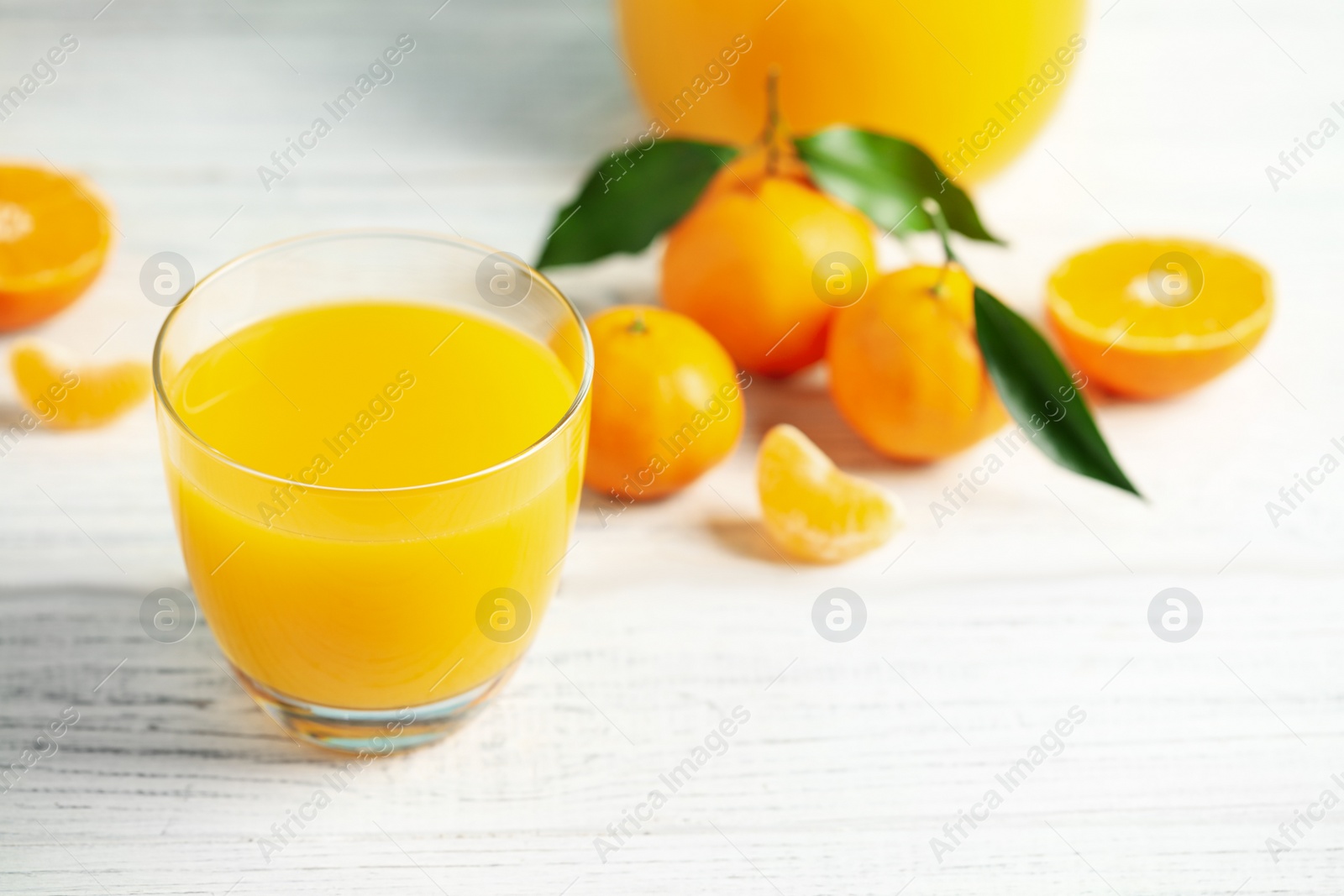 Photo of Glass of fresh tangerine juice and fruits on white wooden table