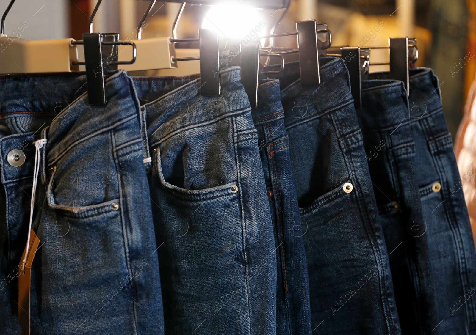 Photo of Modern jeans hanging on clothing rack in shop, closeup