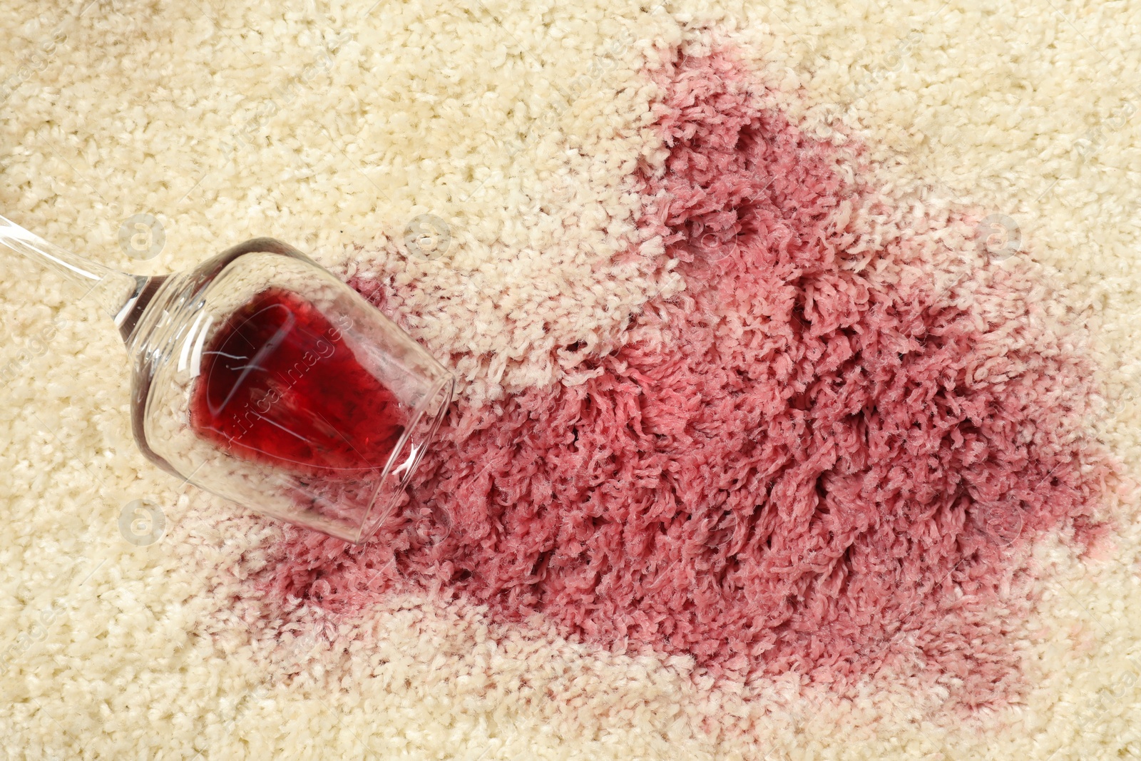 Photo of Overturned glass and spilled red wine on beige carpet, top view