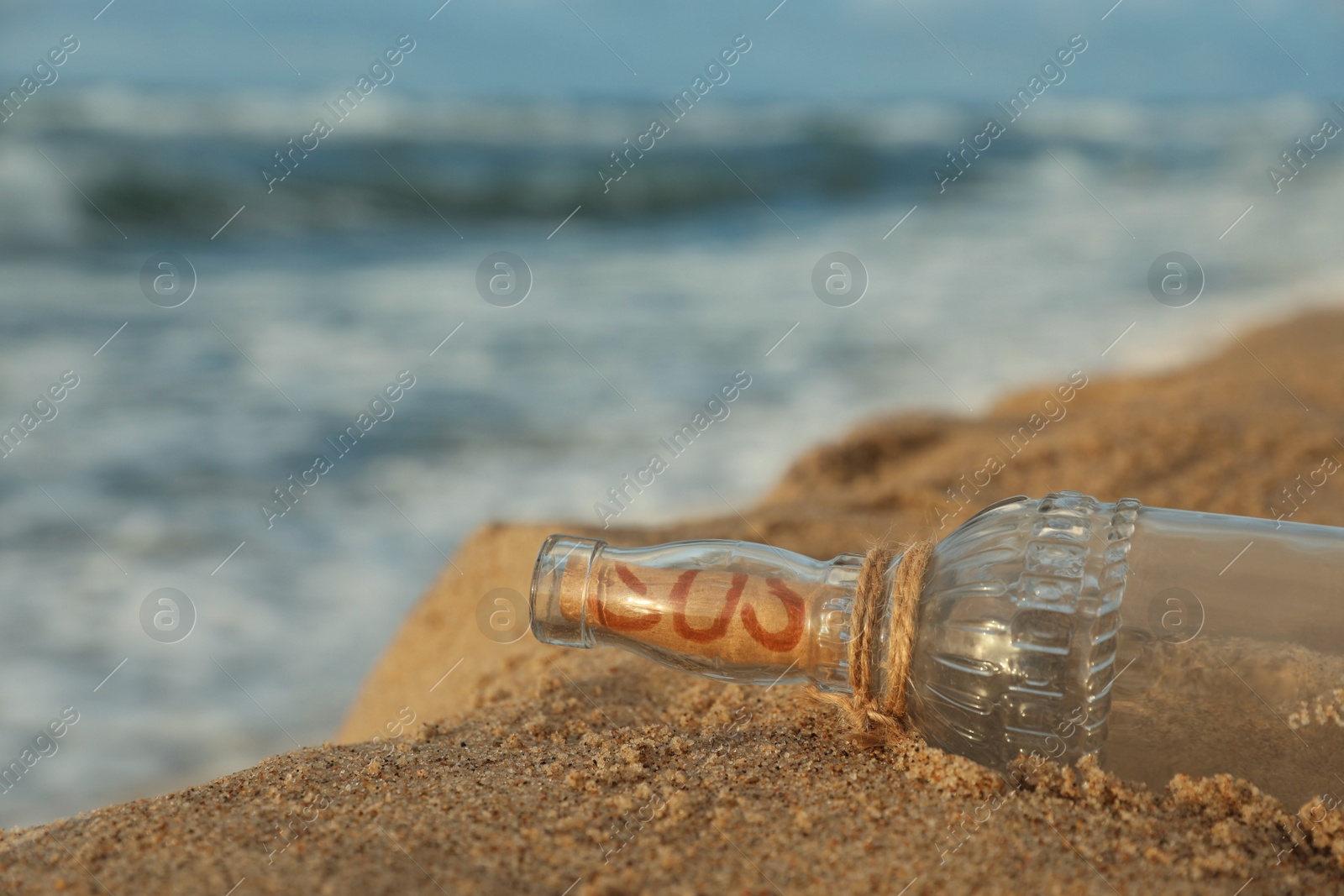 Photo of Glass bottle with SOS message on sand near sea, space for text