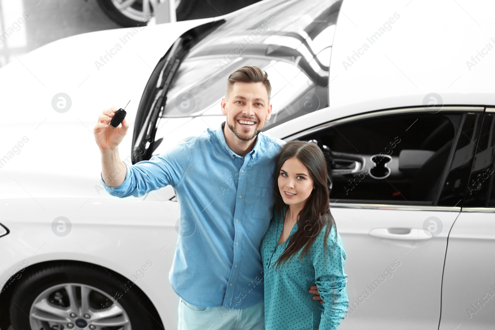 Photo of Young couple with key in salon. Buying new car