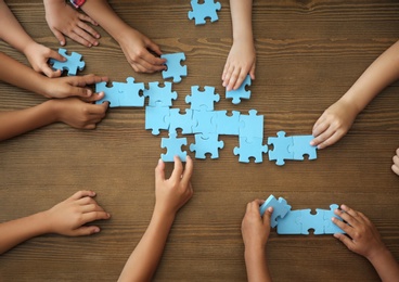 Photo of Top view of little children playing puzzle together at table, focus on hands. Unity concept