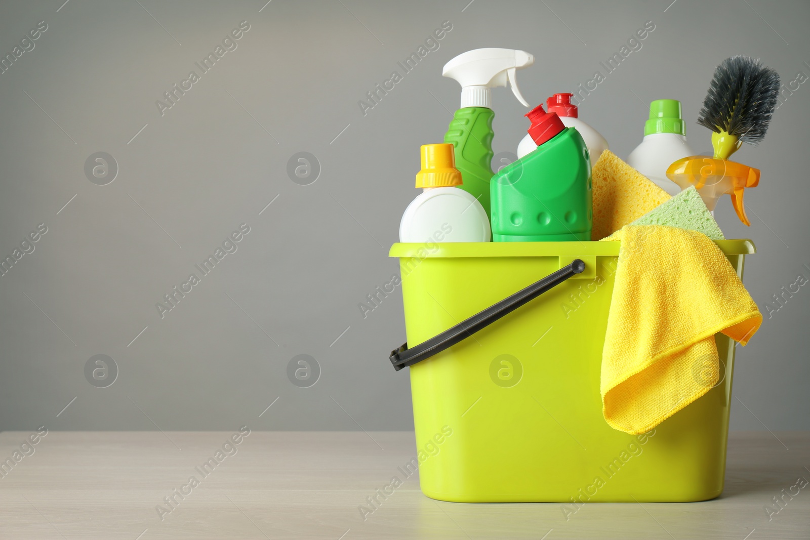 Photo of Bucket with cleaning products and tools on grey table. Space for text