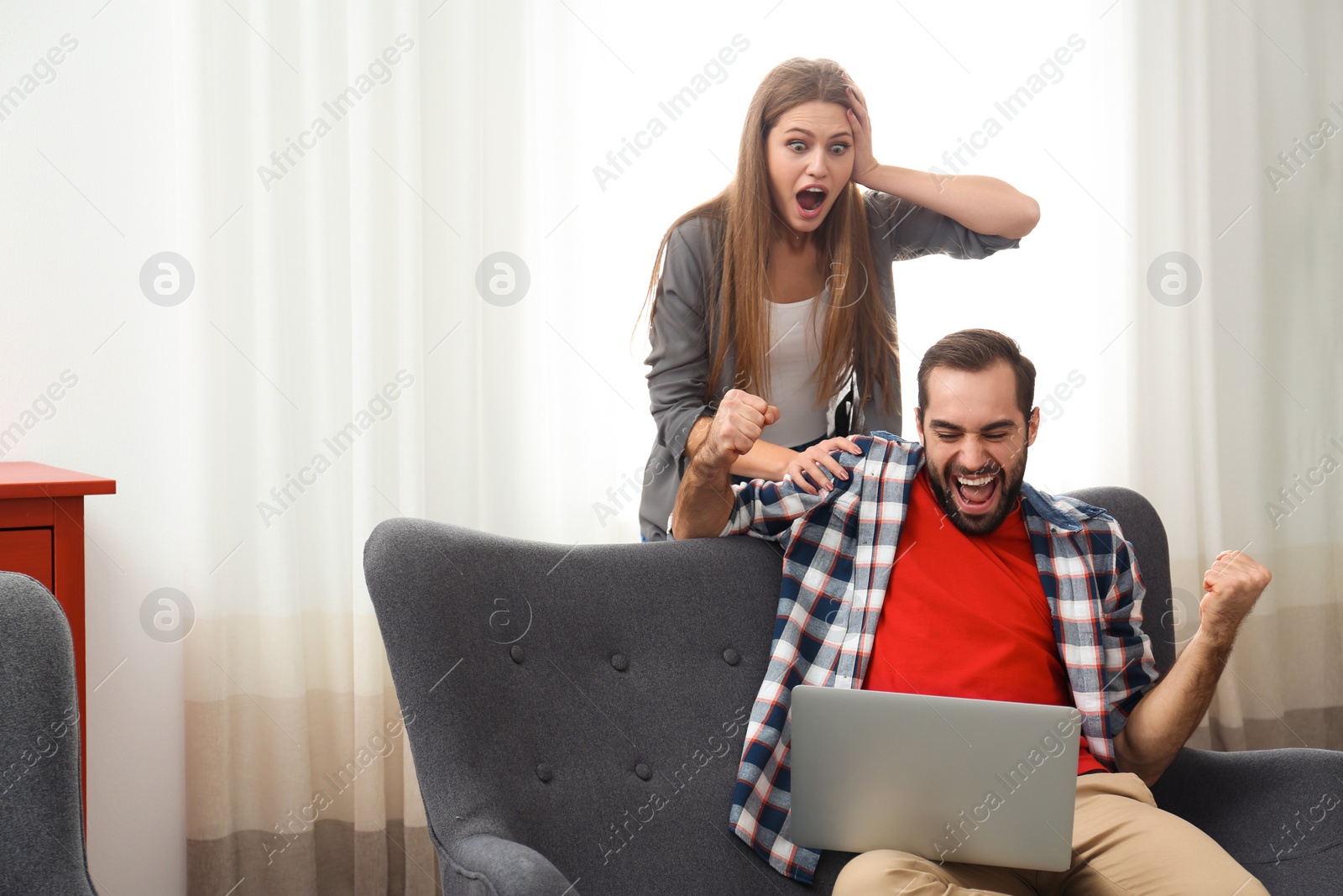 Photo of Emotional young couple with laptop celebrating victory at home