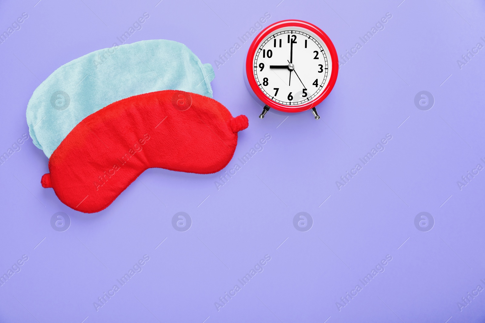 Photo of Soft sleep masks and alarm clock on purple background, flat lay. Space for text