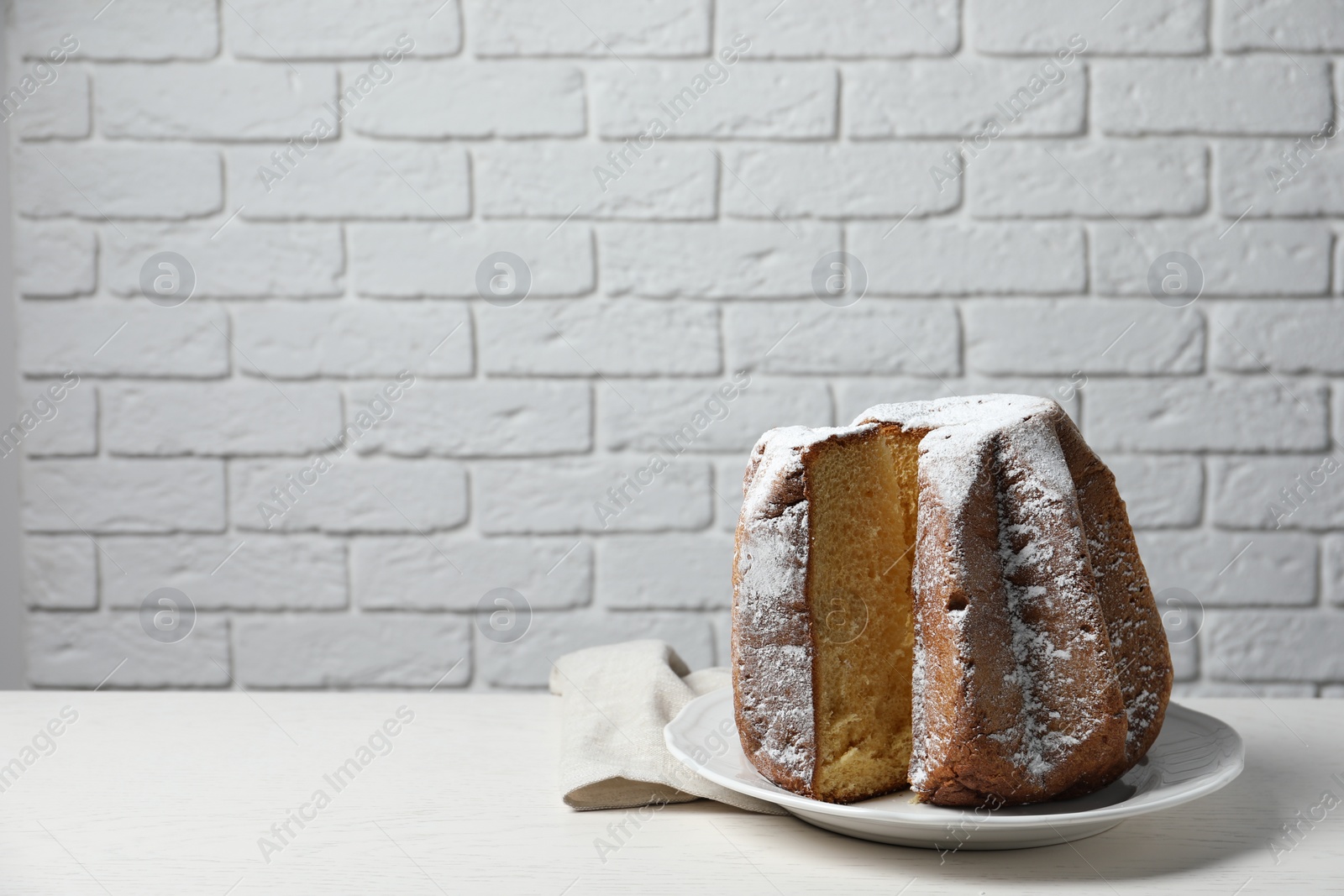 Photo of Delicious Pandoro cake decorated with powdered sugar on white table, space for text. Traditional Italian pastry
