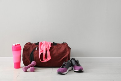 Red bag and sports accessories on floor near light wall, space for text