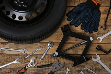 Car wheel, scissor jack, gloves and different tools on wooden surface, flat lay