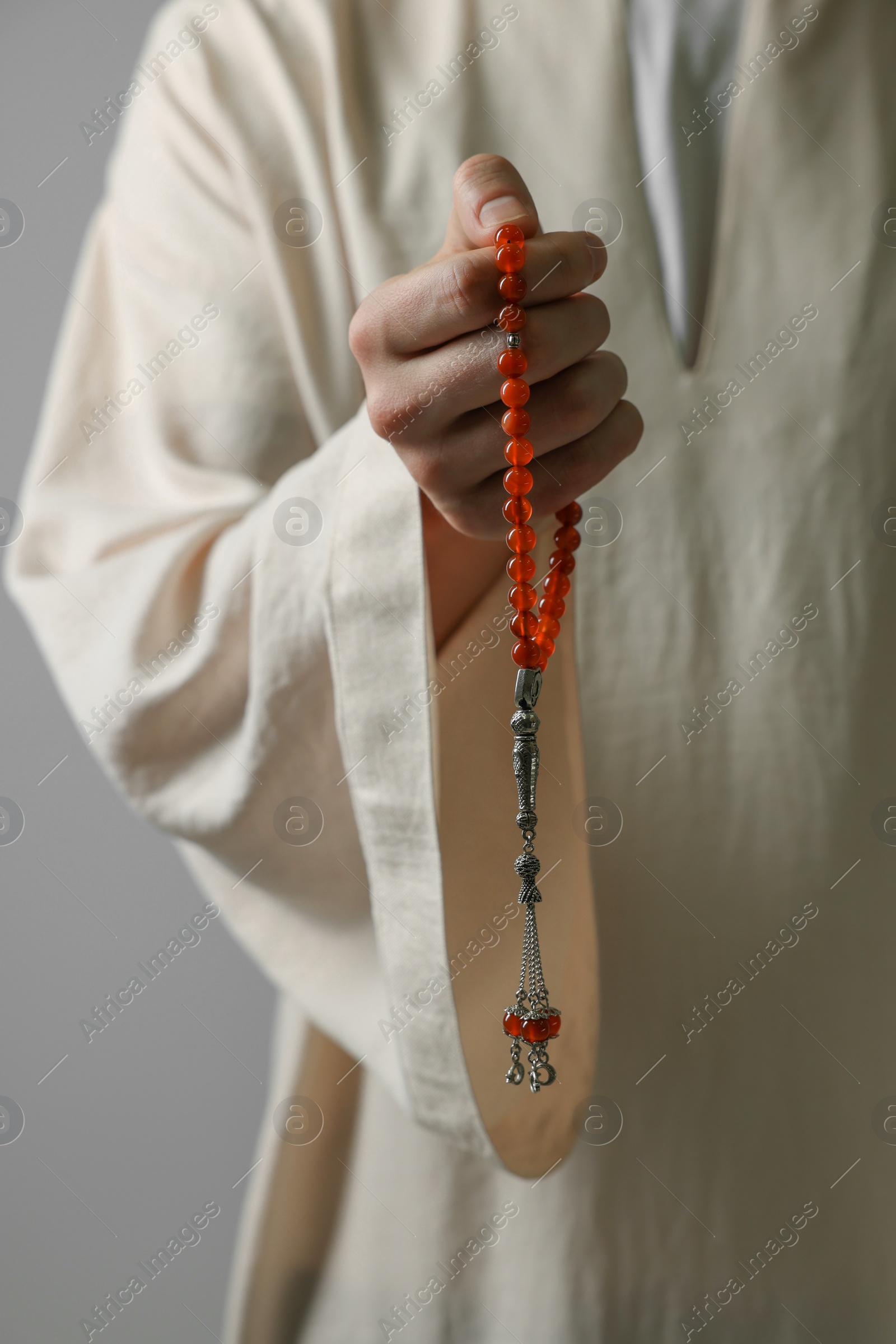 Photo of Muslim man holding misbaha on light grey background, closeup