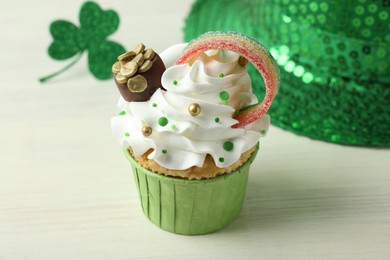 St. Patrick's day party. Tasty cupcake with sour rainbow belt and pot of gold toppers on white table, closeup