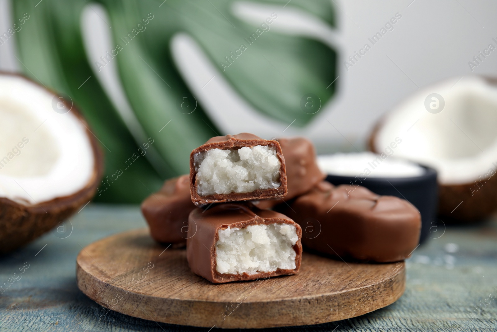 Photo of Delicious milk chocolate candy bars with coconut filling on blue wooden table, closeup. Space for text