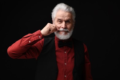 Senior man touching mustache on black background