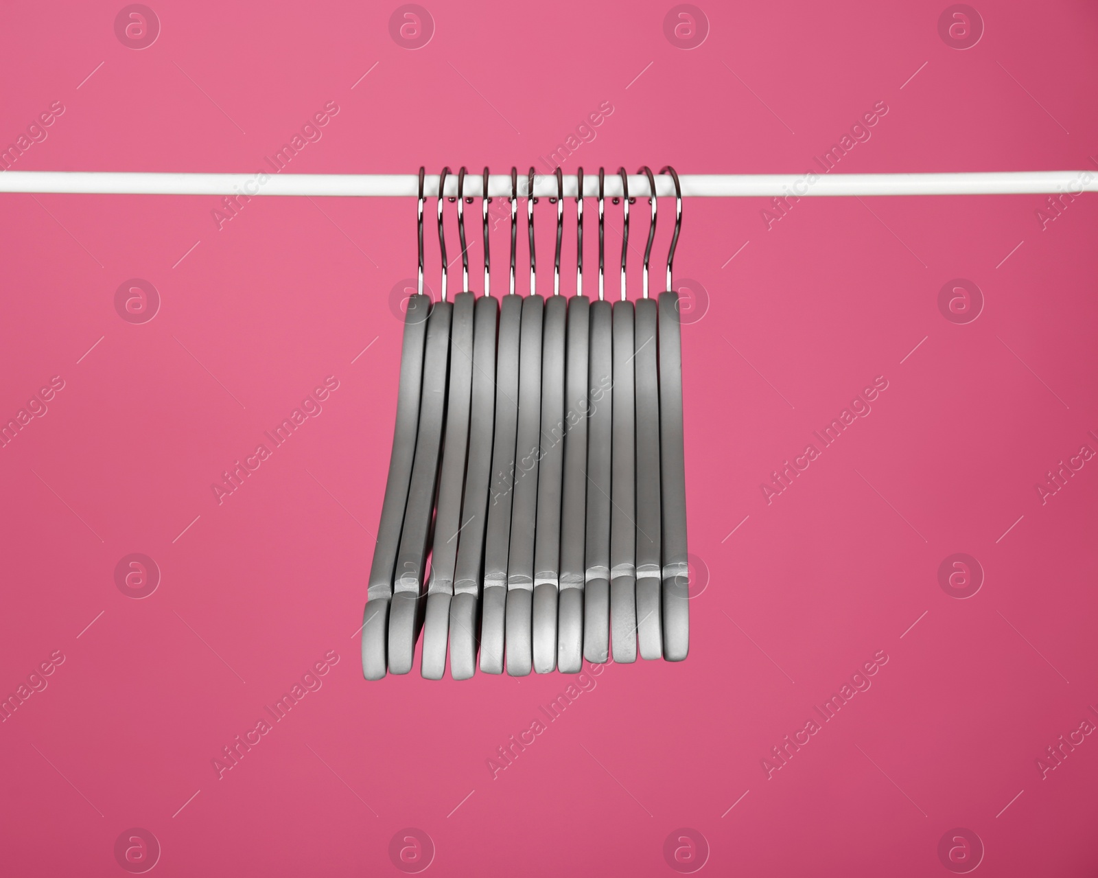 Photo of Empty clothes hangers on metal rail against color background