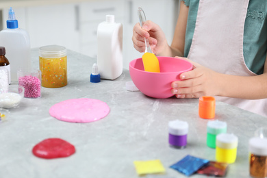 Photo of Little girl mixing ingredients with silicone spatula at table, closeup. DIY slime toy