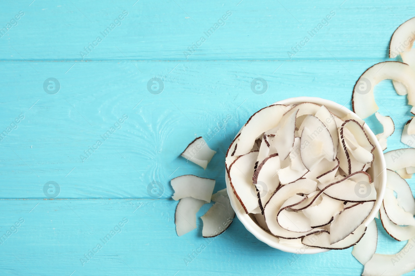 Photo of Tasty coconut chips on light blue wooden table, flat lay