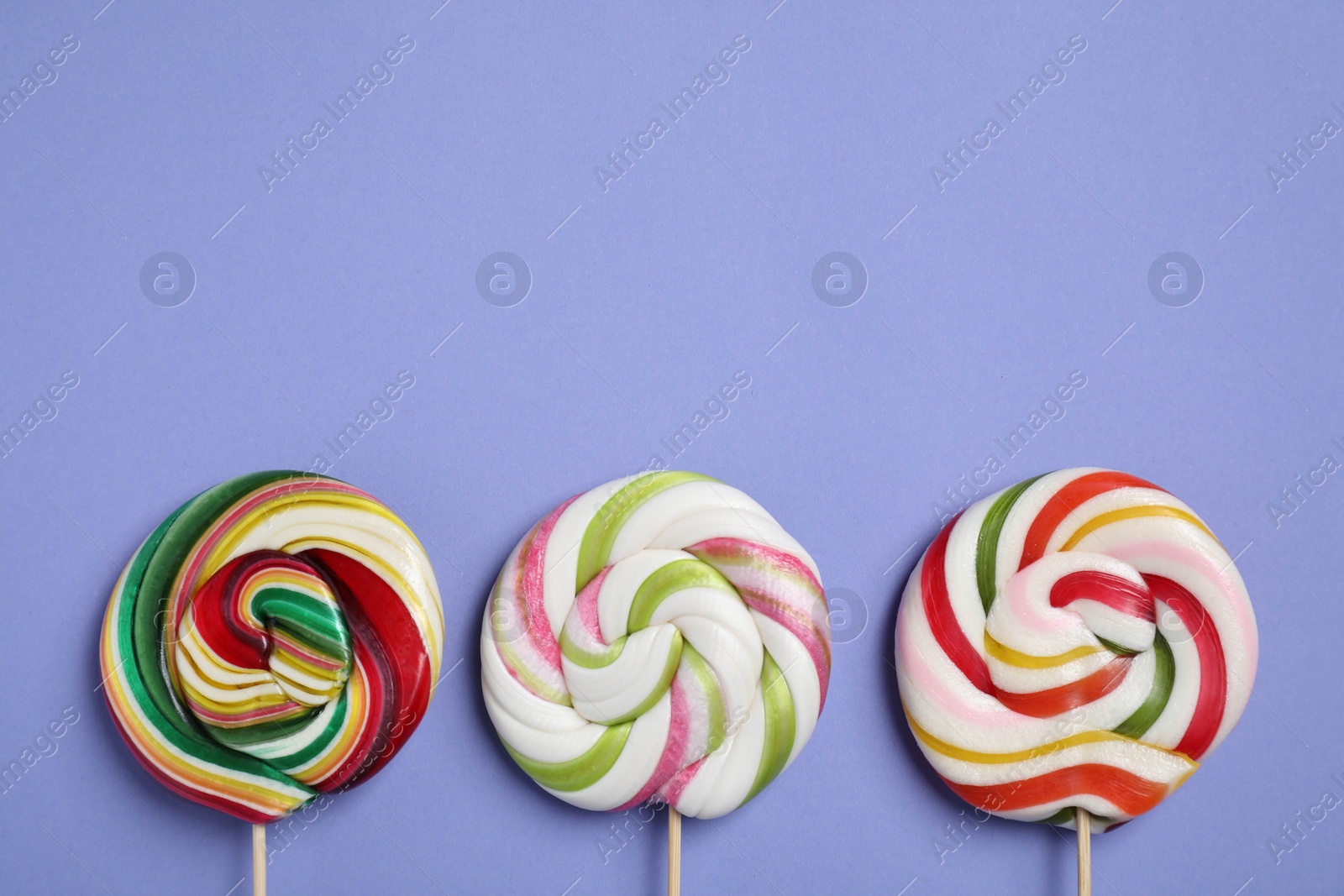 Photo of Sticks with different colorful lollipops on violet background, flat lay. Space for text