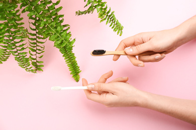 Photo of Woman holding natural bamboo and plastic toothbrushes on pink background, top view