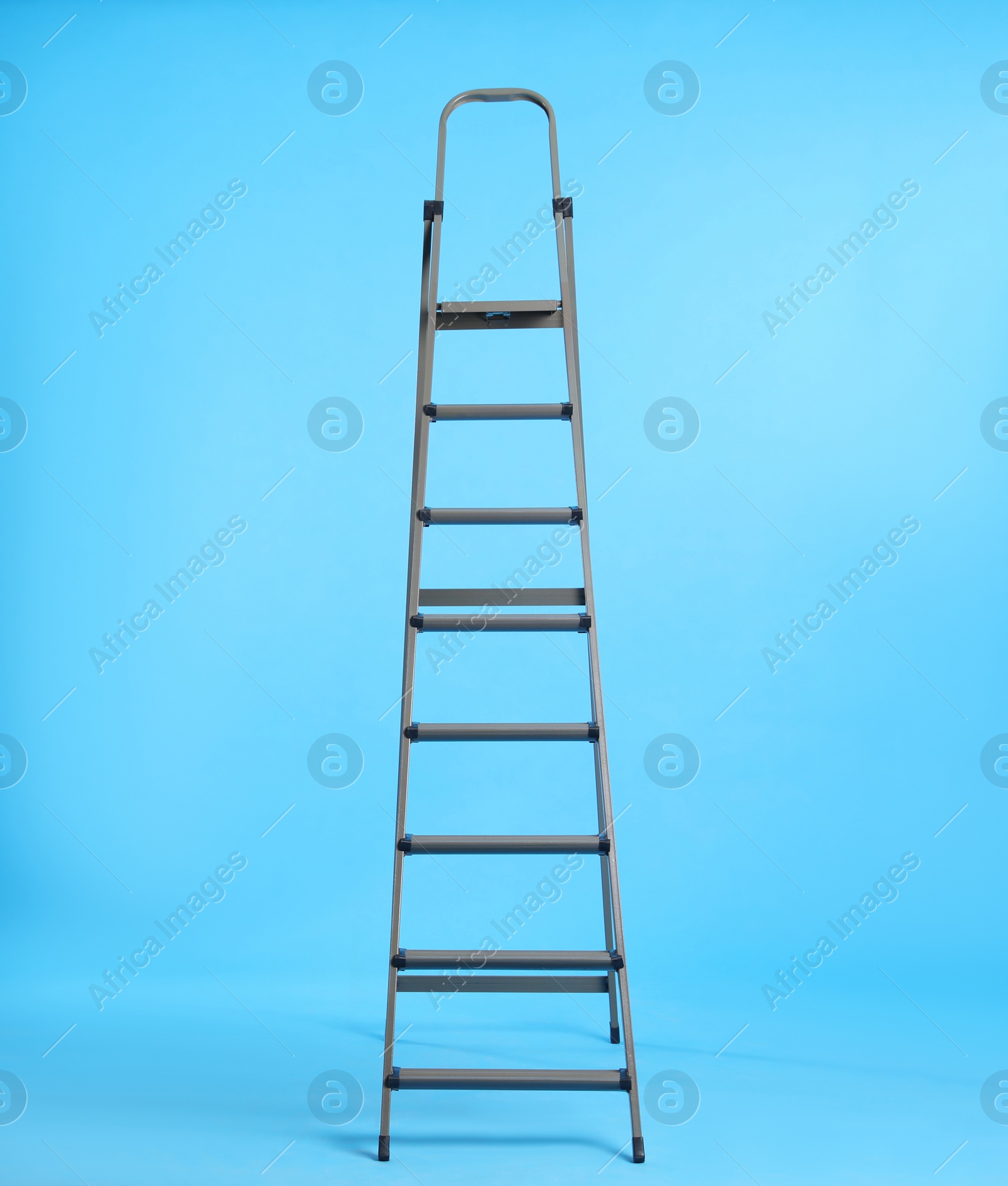 Photo of Metal stepladder on light blue background. Space for text