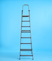 Photo of Metal stepladder on light blue background. Space for text