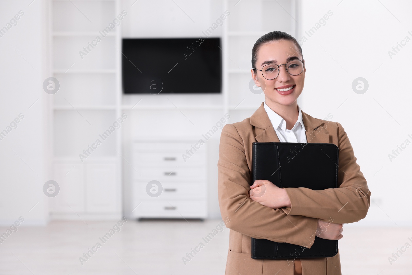 Photo of Happy real estate agent with leather portfolio indoors. Space for text