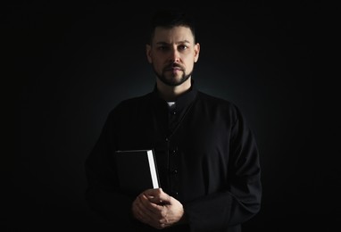 Photo of Priest in cassock with Bible on dark background