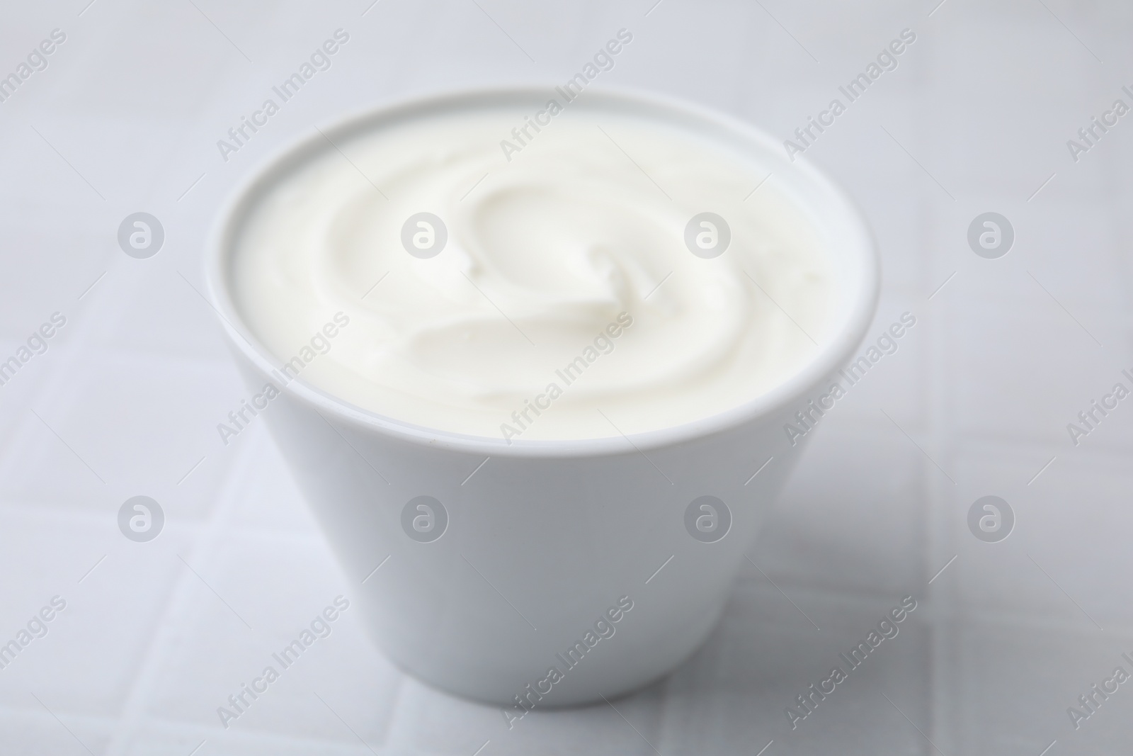 Photo of Delicious natural yogurt in bowl on white tiled table, closeup